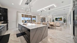 Una cocina moderna con una isla de mármol, armarios negros e iluminación colgante.
