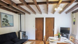 A cozy living room with a wooden ceiling, a black sofa, a small table, and a dining area with a table set for two. - Stunning private villa for 6 guests with WIFI, TV and pets allowed (Le Porge)