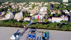 An aerial view of a coastal town with residential buildings, a beach area with umbrellas and sun loungers, and a clear view of the sea.