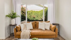 Un salon chaleureux avec un canapé en cuir marron, des coussins blancs, un plaid beige et une petite plante en pot.