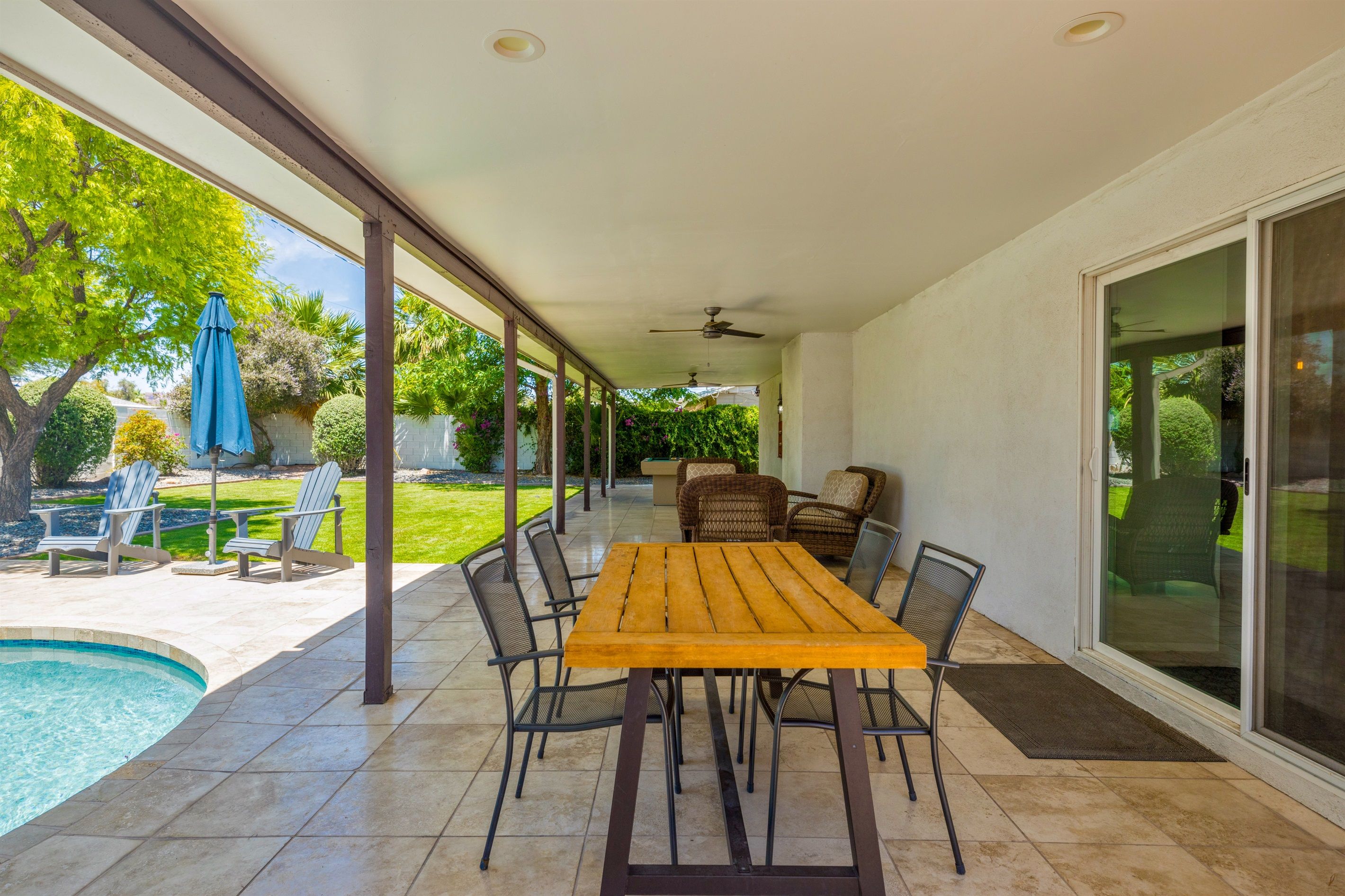 A covered patio with a pool, outdoor seating, and a view of the garden.