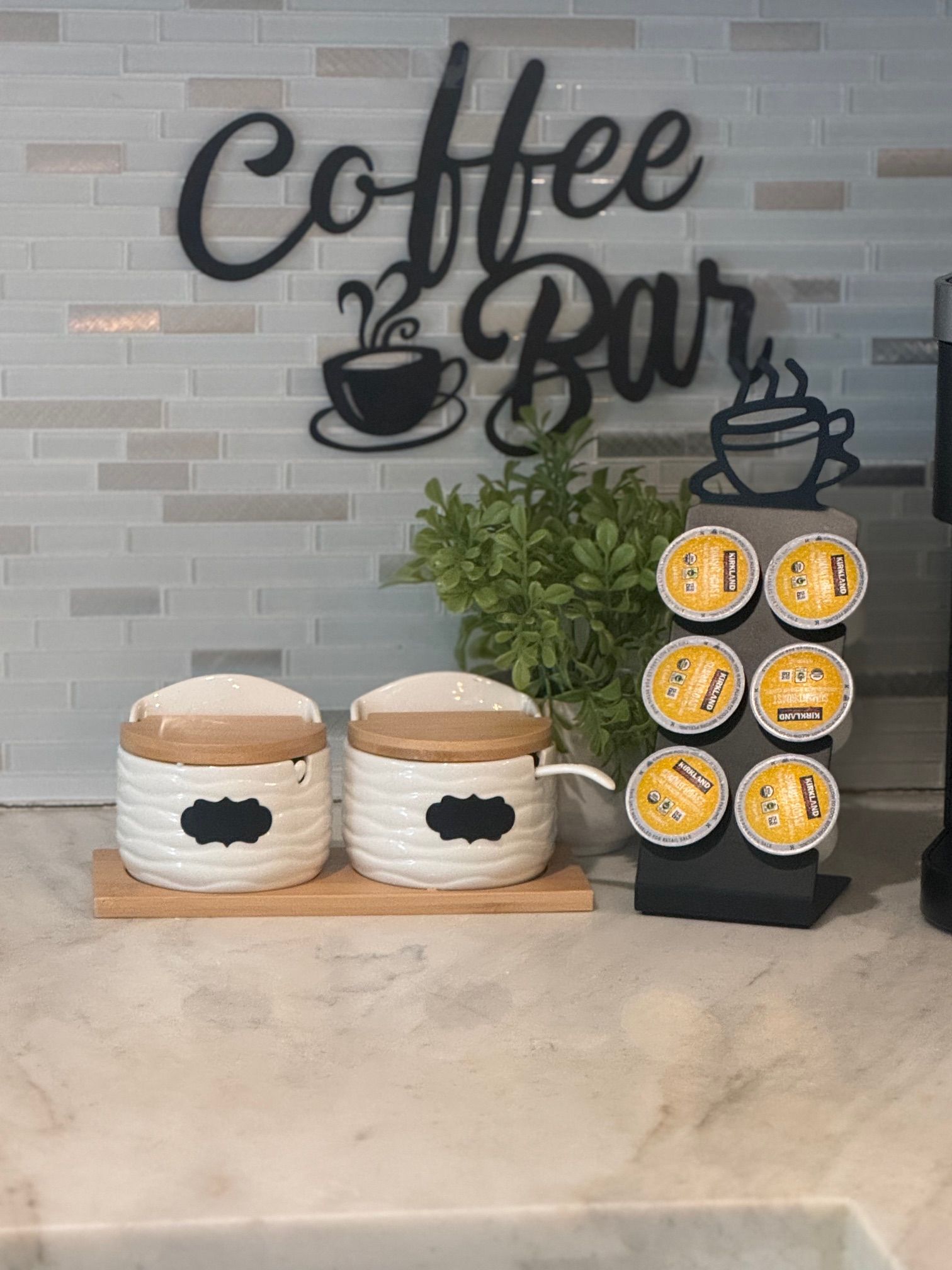 Two ceramic coffee containers with lids on a wooden board, a coffee-themed wall decoration, and a display stand with coffee capsules.