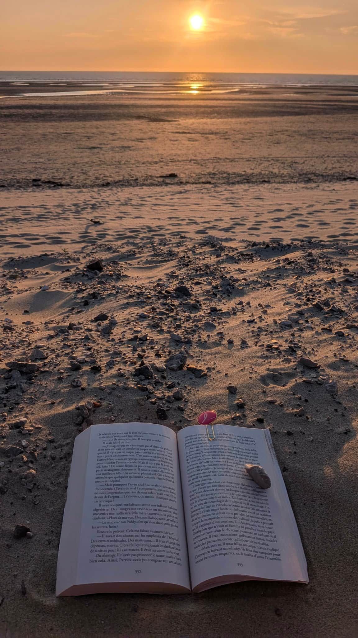 Ein offenes Buch am Sandstrand, im Hintergrund ein untergehender Sonnenuntergang.