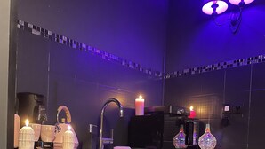 Ett modernt kök med en svart bänkskiva, en kaffebryggare, en brödrost och dekorativa föremål, inklusive ett ljus och glasvaror.