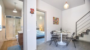 A modern apartment with a glass shower, a dining area with a round table and chairs, a bed with a blue and white patterned bedspread, and a staircase. - 2 bedroom stunning apartment in Ogliastro Marina (Ogliastro Marina)