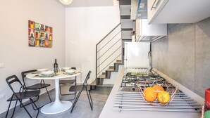 A compact kitchen with a gas stove, a sink, and a fruit basket. There is a dining area with a table and chairs. A colorful artwork is on the wall. - 2 bedroom stunning apartment in Ogliastro Marina (Ogliastro Marina)