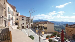 A narrow street with buildings on both sides, a small plaza with outdoor seating, and a mountain view in the background. - 2 bedroom stunning apartment in Ogliastro Marina (Ogliastro Marina)