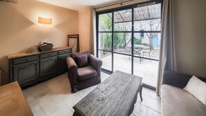 Une pièce comprenant un canapé, une table en bois, un meuble et une grande porte-fenêtre coulissante donnant sur un espace extérieur avec une table et des chaises.