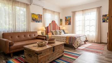 Una habitación con un sofá de cuero marrón, un aparador de madera, una cama con colcha a rayas y dos lámparas de pared.
