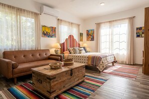 Una habitación con un sofá de cuero marrón, un aparador de madera, una cama con colcha a rayas y dos lámparas de pared.