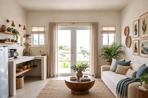 A modern living room with a coffee table, sofa, and kitchen area with appliances. - La Optimista Boutique Hotel & Concierge (Todos Santos)