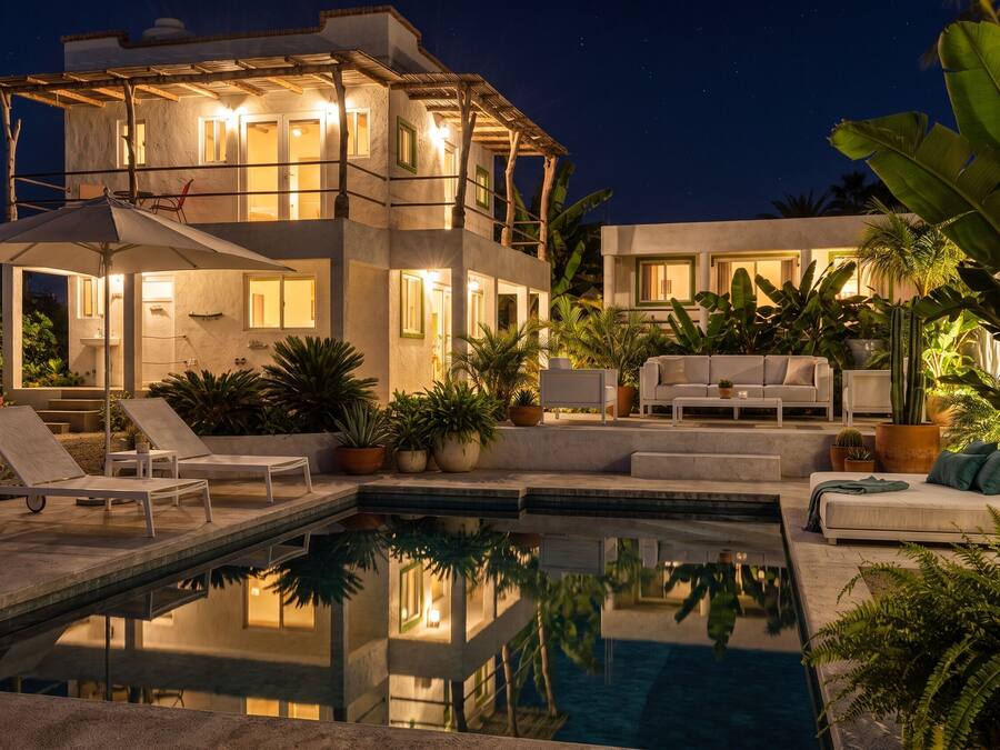 Una casa de dues plantes amb piscina, mobles d'exterior i diverses plantes.