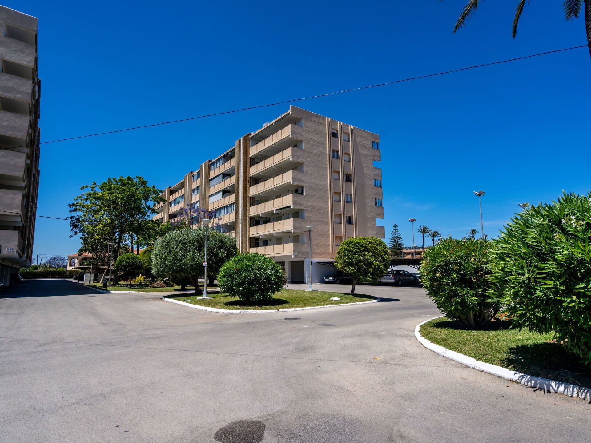 Un edificio residencial de varios pisos con balcones, rodeado de vegetación y un cielo despejado.