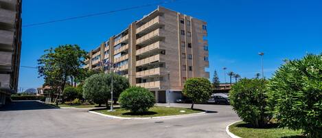Un edificio residencial de varios pisos con balcones, rodeado de vegetación y un cielo despejado.