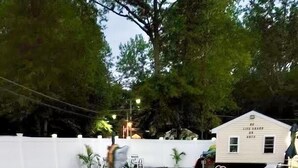 A swimming pool with a metal ladder, surrounded by a white fence and trees. There is a small building labeled "NO LIFEGUARD ON DUTY" in the background. - The Weekender Unit #5 (Geneva-on-the-Lake)