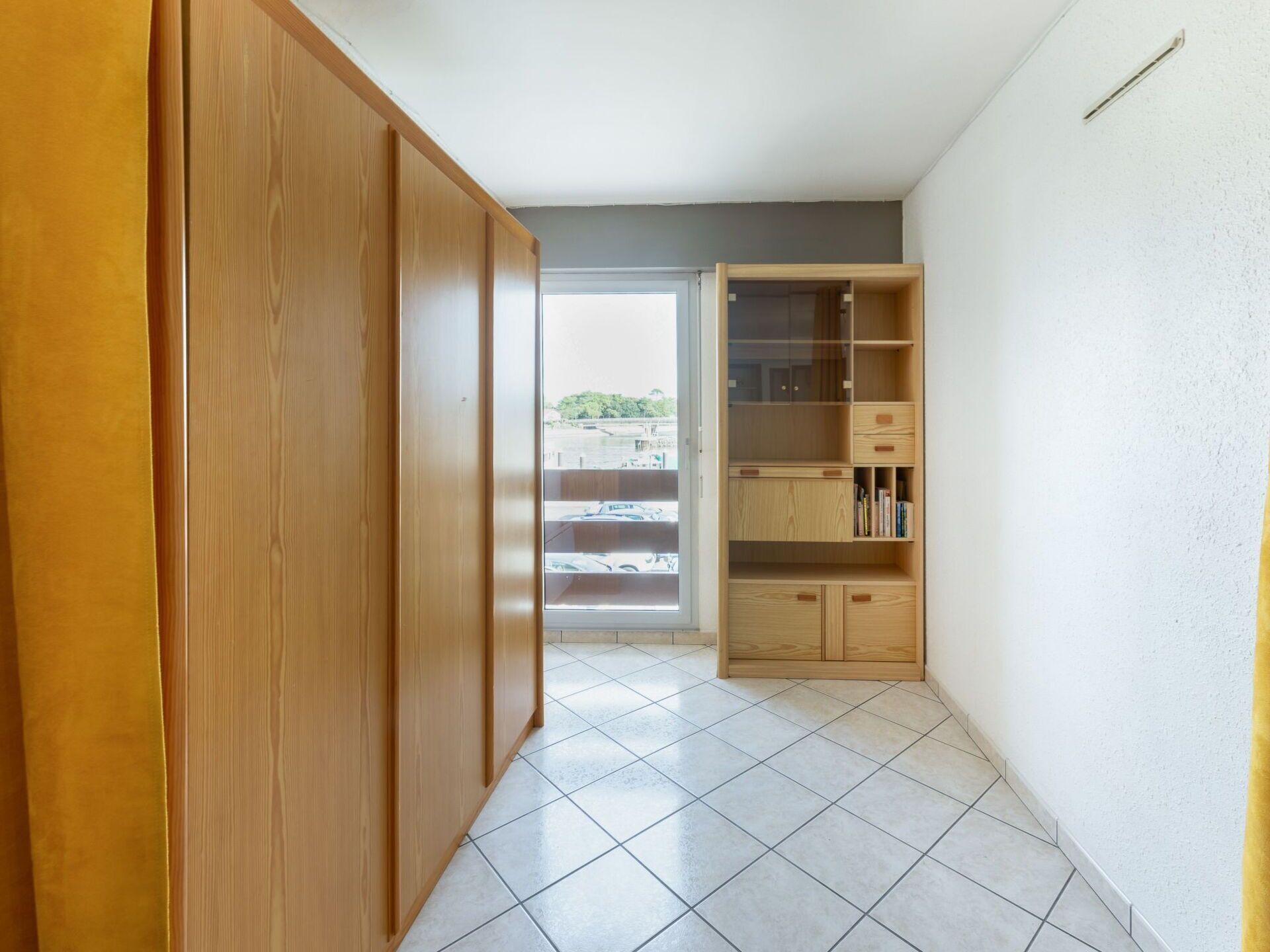 A hallway with a wooden wardrobe, a sliding glass door leading to a balcony, and a built-in wooden shelving unit.