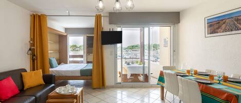 A modern hotel room with a sofa, dining table, and a balcony with a view.