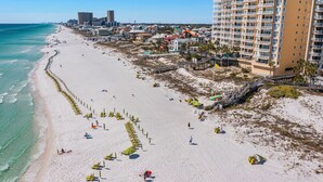 A beach with rows of beach chairs and umbrellas, a boardwalk, and a tall hotel building.