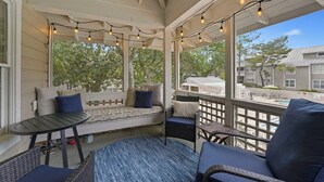 A covered porch with seating, string lights, and a view of a swimming pool and buildings.