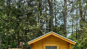 A small wooden cabin with a single door and window, surrounded by a gravel path and greenery. - Luxury Winter Gateaway (Nestleton Station)