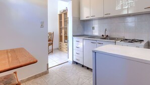 A modern kitchen with white cabinets, a gas stove, and a wooden dining table. - Cosy apartment for 2 people with A/C, WIFI, TV and terrace (Medulin)