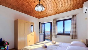 A bedroom with a wooden ceiling, a bed with white linens, a wardrobe, a window with curtains, and a view of the outside.