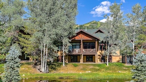 A two-story lodge with a balcony, surrounded by trees and a pond.