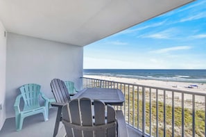 A balcony with two Adirondack chairs and a table, overlooking a beach with a railing. - Four Winds 402 (Orange Beach)