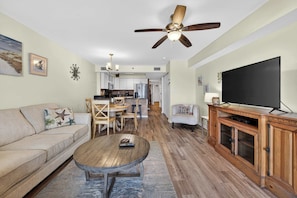 A living room with a sofa, coffee table, TV, and a dining area with chairs and a table.