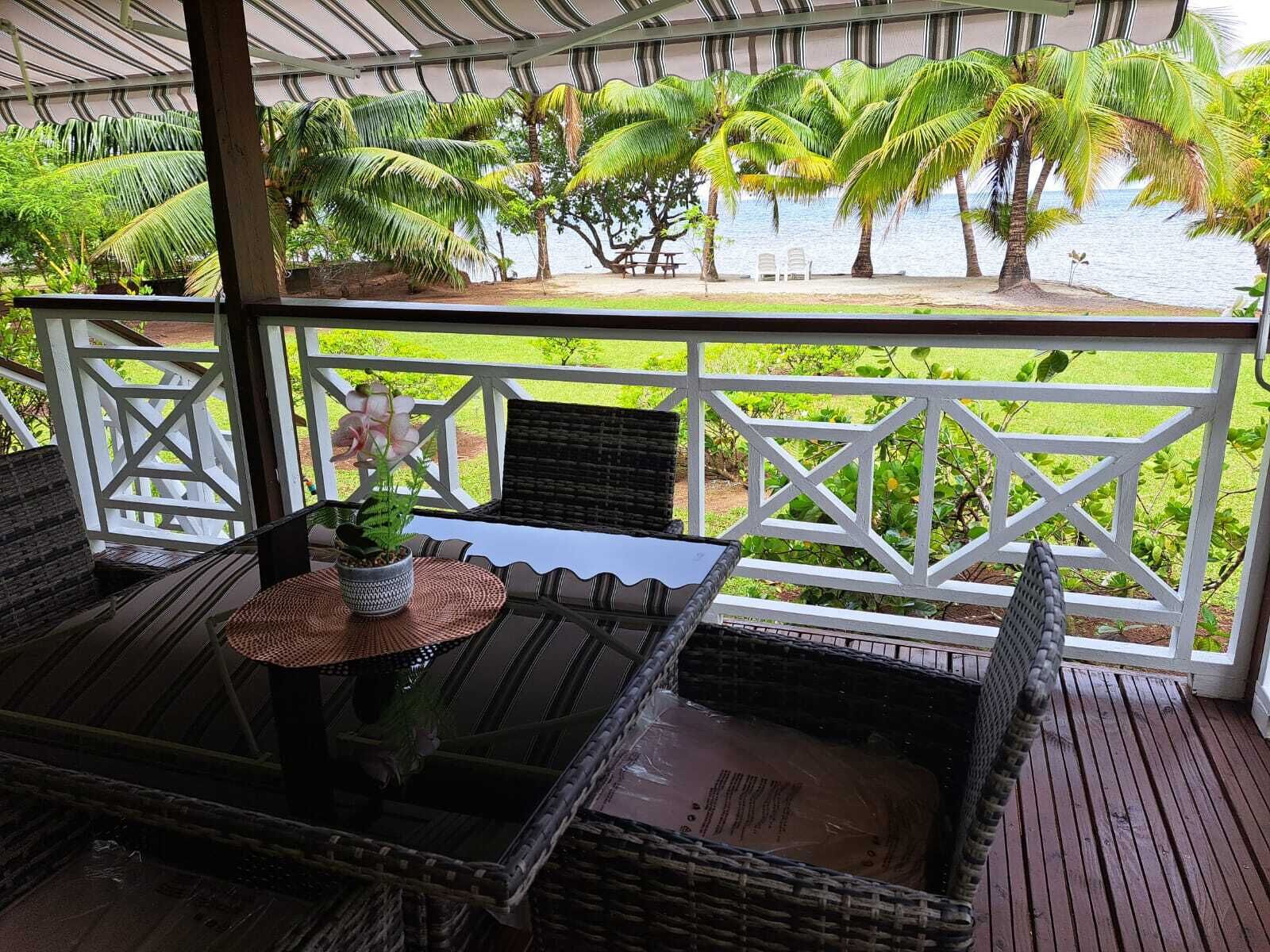 Ein überdachter Außenbereich mit Korbmöbeln und Blick auf Palmen und Wasser.
