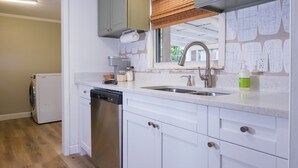 A kitchen with white cabinets, a dishwasher, a sink with a faucet, and a window with a view of greenery.