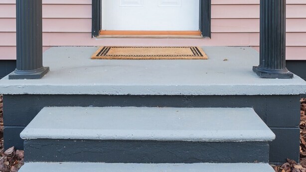 A white door with a decorative glass panel, flanked by two black columns, and a small light fixture above the door.