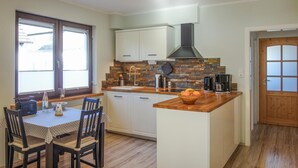 Eine kleine Küche mit weißen Schränken, einer Arbeitsplatte aus Holz und einer Essecke mit Tisch und Stühlen. Die Rückwand ist mit Stein verkleidet.