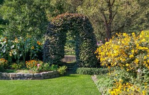A garden with a stone pathway, a green archway, and various flowering plants.