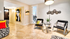 En moderne stue med en sofa med zebra-mønster, to sorte læderstole med dekorative puder, et lille rundt bord, en gulvlampe og et stort abstrakt maleri.