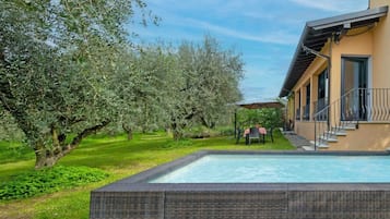 Ein Poolbereich mit Korbmöbeln, blauem Himmel und Olivenbäumen.