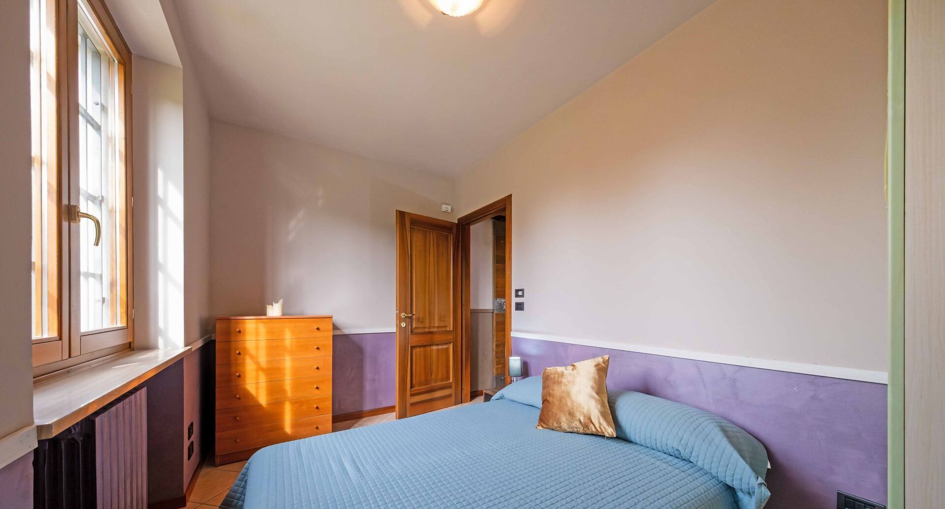 Een slaapkamer met een bed, een dressoir, een deur en een raam.