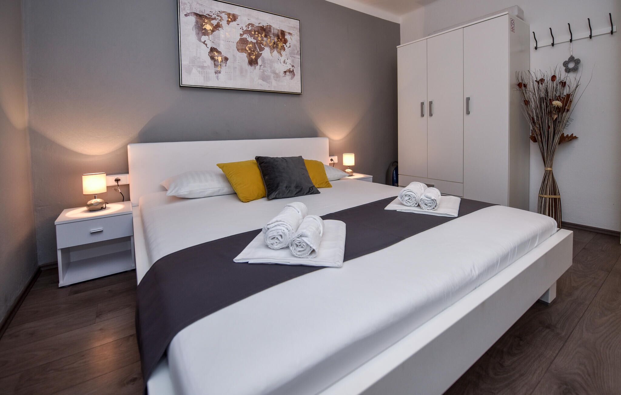 A modern hotel room with a large bed, two bedside tables, a wardrobe, and a world map artwork on the wall.