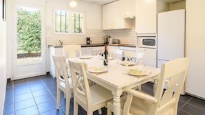 Una cocina moderna con armarios blancos, una mesa de comedor para cuatro personas y un ventanal que proporciona luz natural.
