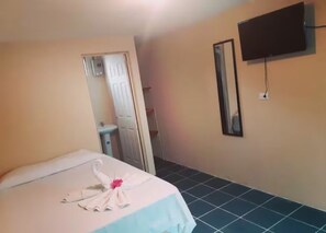 Une chambre d’hôtel avec un lit, un téléviseur fixé au mur et une salle de bain visible à travers une porte ouverte.