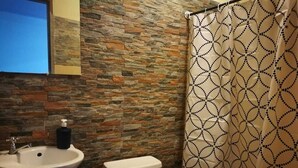 A bathroom with a stone wall, a sink, a toilet, and a patterned shower curtain. - ¡Acogedora habitación privada en el corazón de Quepos! (Quepos)
