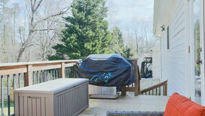 Ein überdachter Grill im Freien auf einer Holzterrasse mit einem Korbstuhl und einem Tisch.