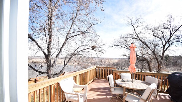 A wooden deck with outdoor furniture, including chairs and a table, overlooking a body of water.