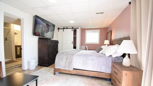 A bedroom with a bed, bedside tables, a TV mounted on the wall, and a window.