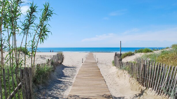 Une promenade en bois menant à une plage, avec un ciel dégagé.