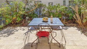 Une terrasse avec une table et des chaises, un saladier rempli de fruits et une bouteille de vin.