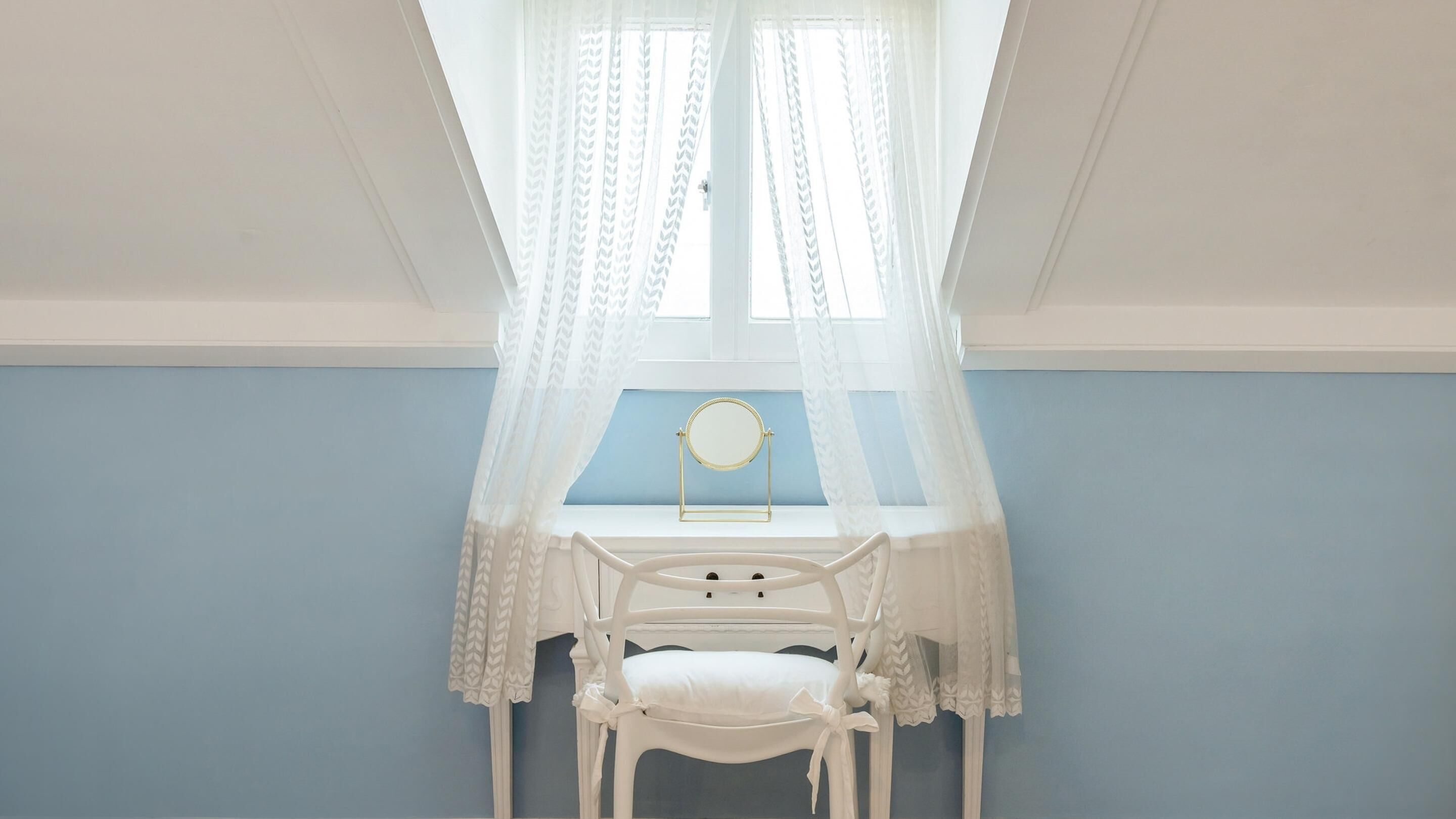 A room with a blue wall, a white desk with a mirror, and a white chair.