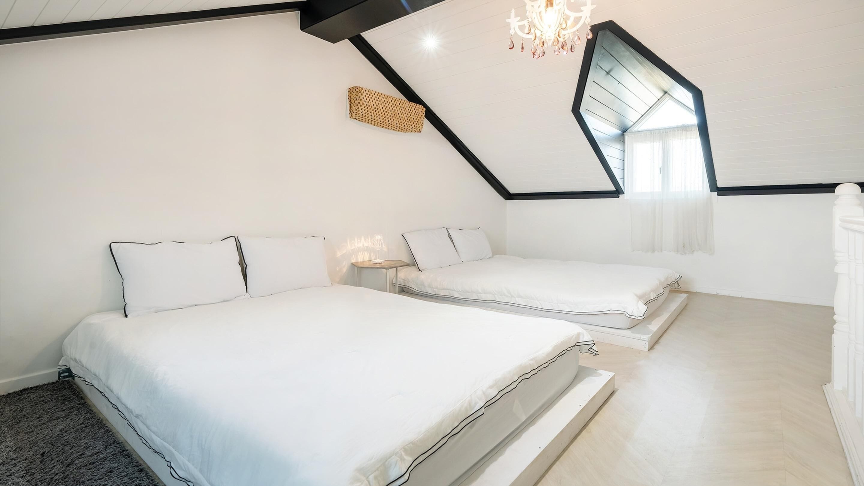 A bedroom with two beds, a chandelier, and a sloped ceiling.