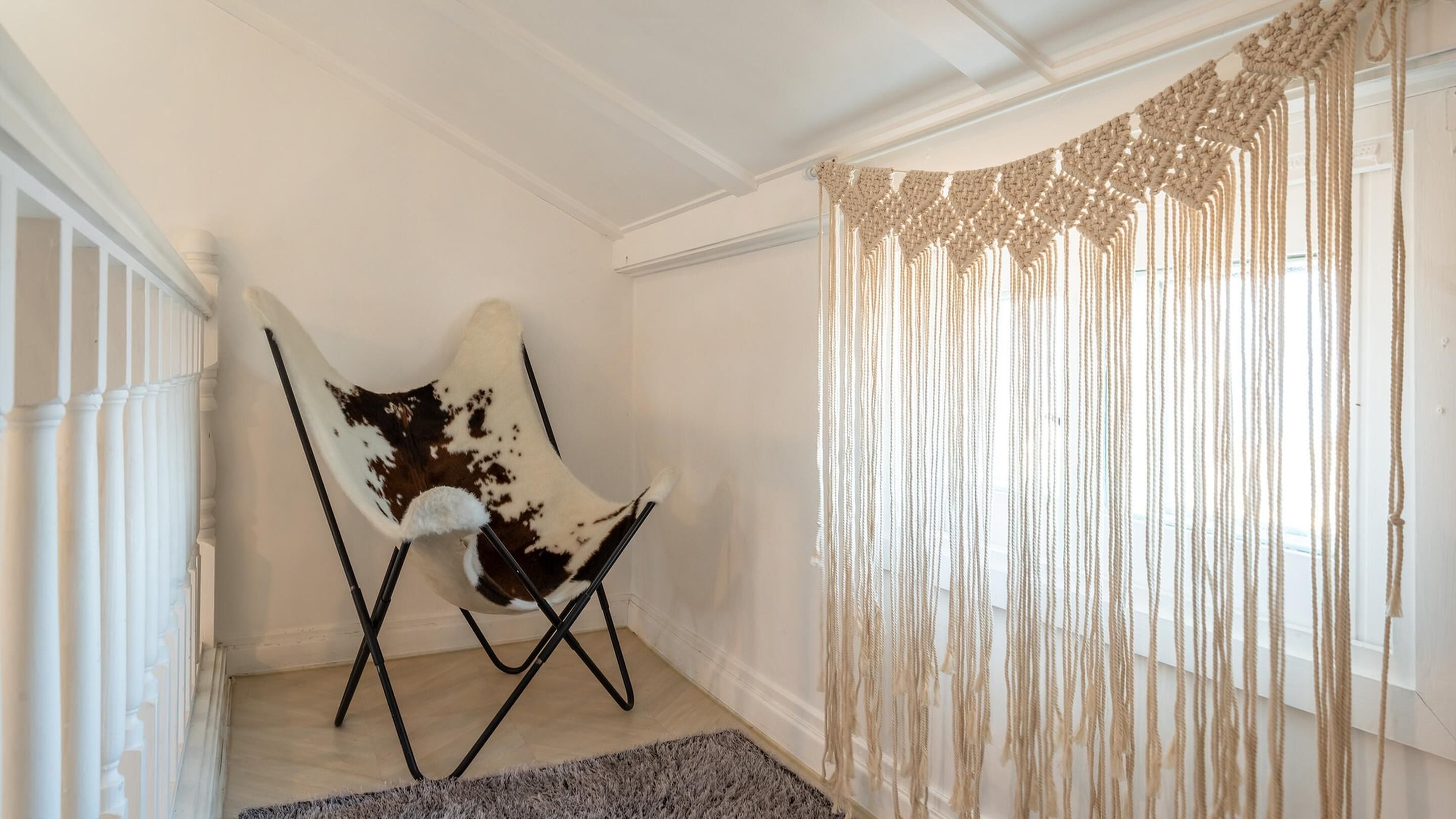 A room with a white chair, a macrame curtain, and a wooden floor.