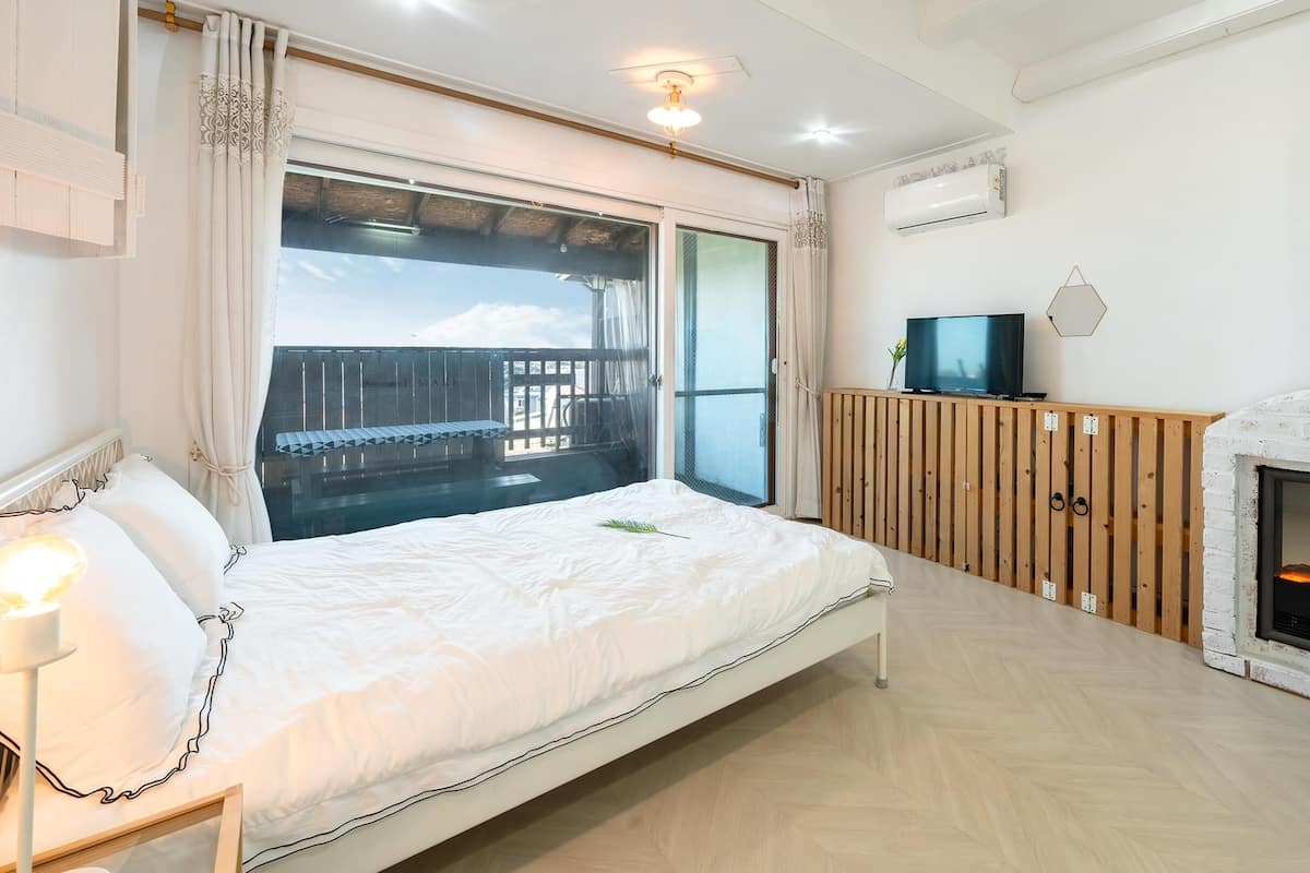 A bedroom with a bed, a TV, a fireplace, and a balcony with a view.